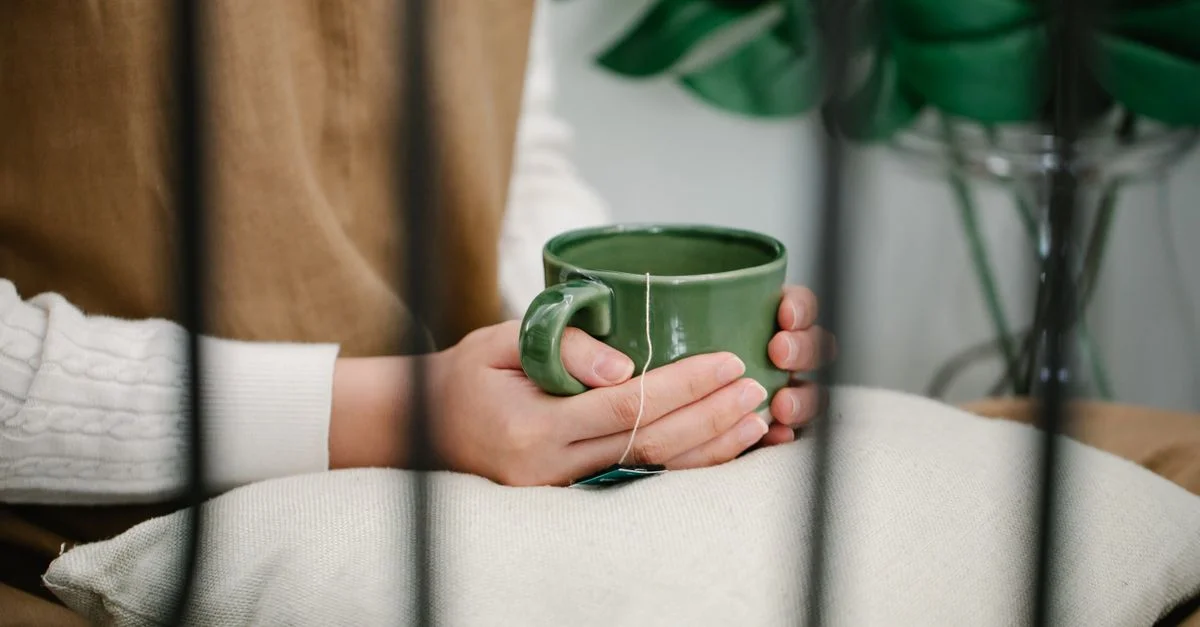 Un moment de détente à l'intérieur avec des mains tenant une tasse verte, reposant sur un coussin.