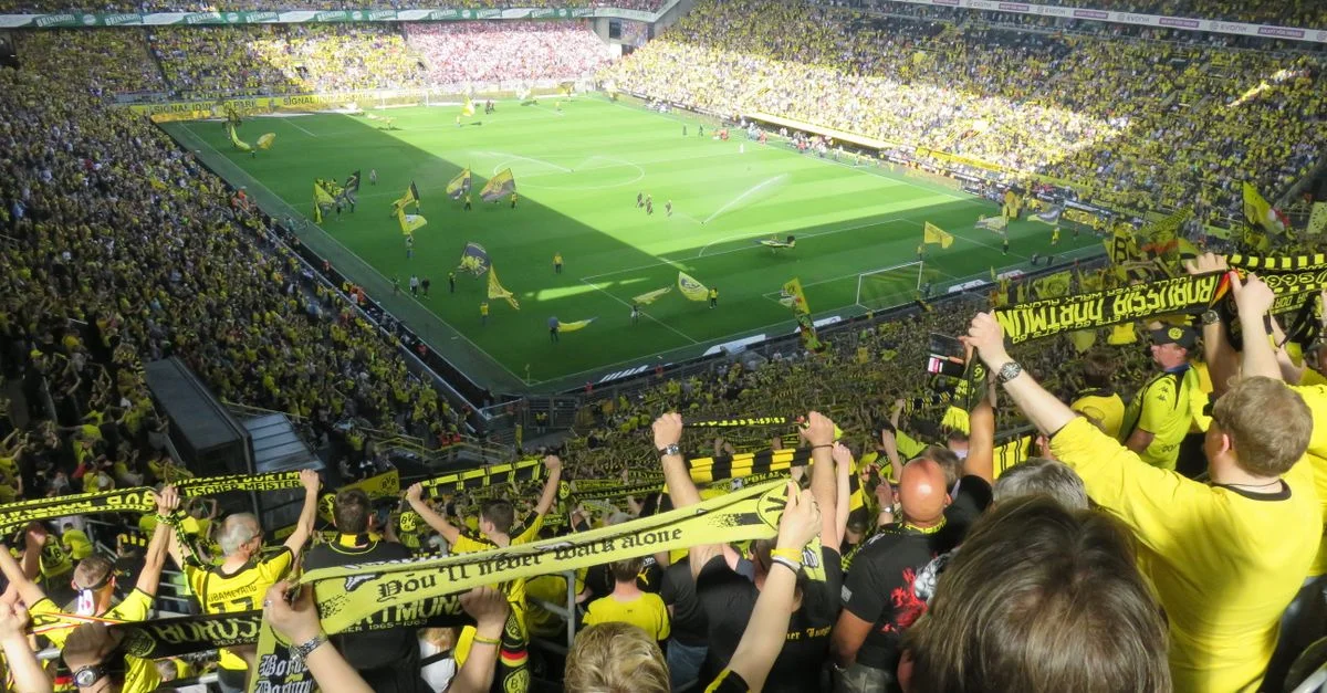 Des fans enthousiastes de Borussia Dortmund applaudissant lors d'un match de football intense au stade.