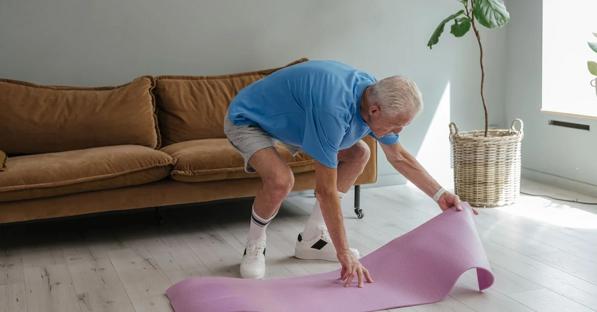 Un homme âgé prépare son tapis de yoga à l'intérieur, incarnant un mode de vie sain.