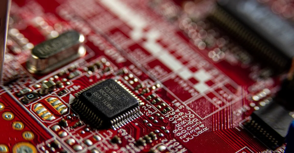 Prise de vue macro détaillée d'une carte de circuit rouge, mettant en avant des composants électroniques et des microprocesseurs.