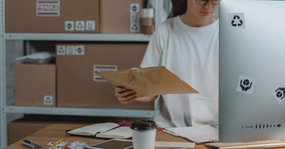 Femme triant des colis à son bureau dans un bureau de logistique, démontrant une organisation efficace de l'espace de travail.