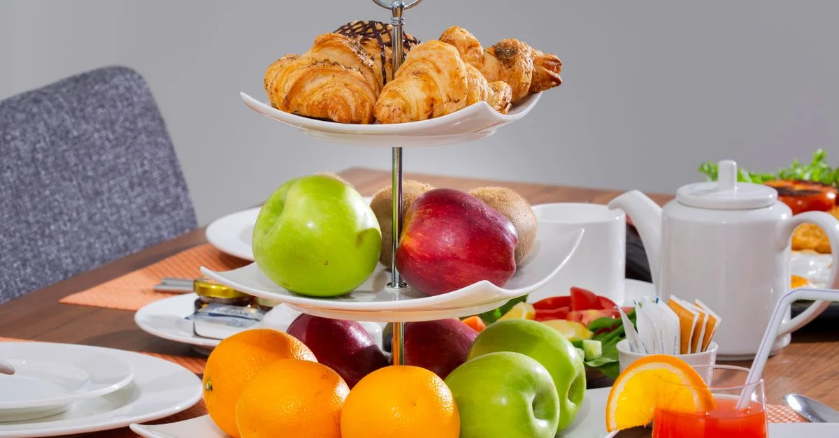 Un plateau à trois niveaux avec des croissants frais et des fruits sur une table de petit-déjeuner. Lumineux et attrayant.
