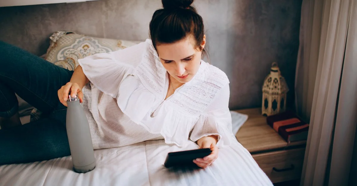 Une jeune femme, dans un cadre décontracté, lit sur une tablette, allongée sur un lit à l'intérieur.