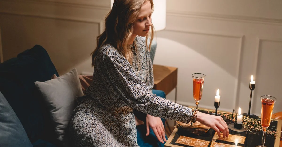Femme adulte avec les cheveux longs jouant aux cartes sur une table, avec des boissons et des bougies.