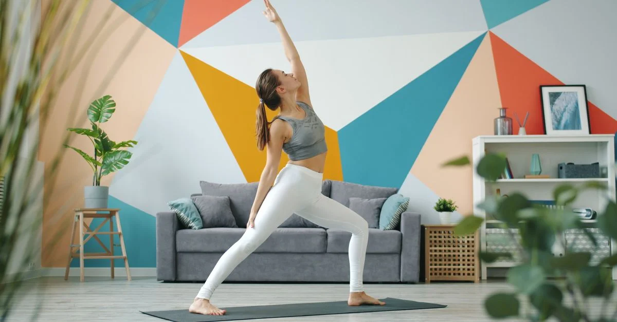 Une jeune femme pratique le yoga dans un studio moderne aux murs décorés de motifs géométriques colorés.