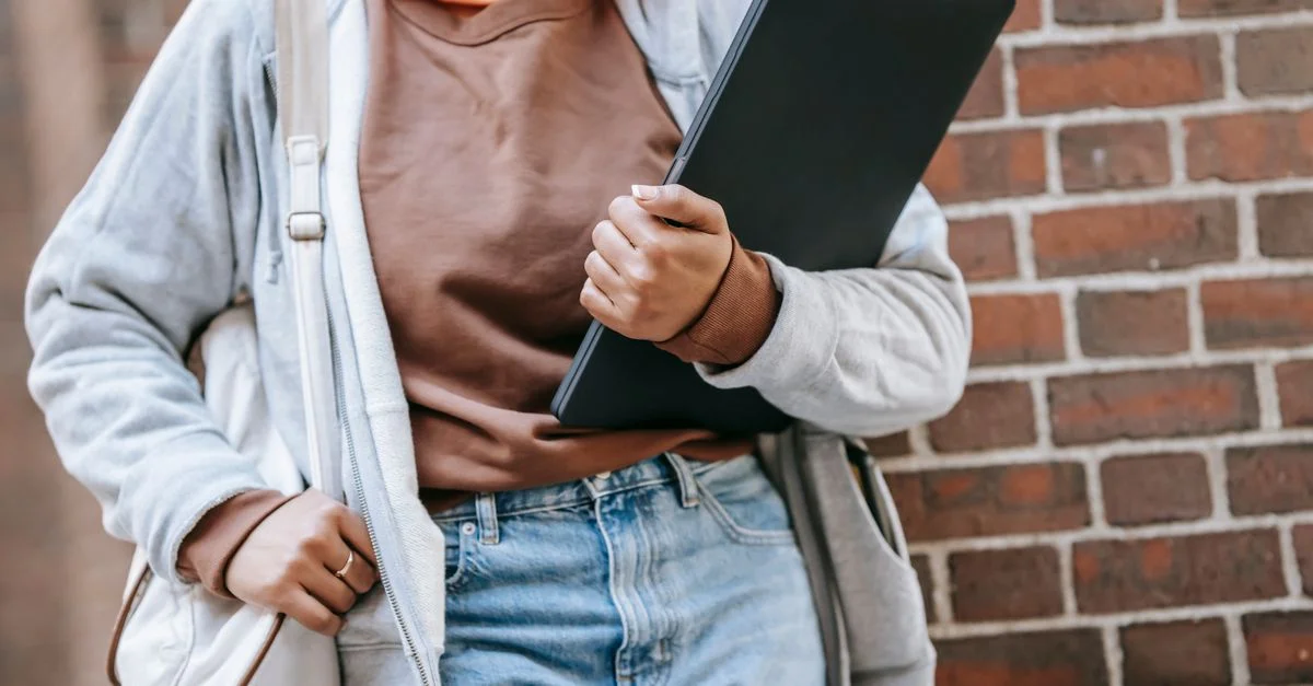 Femme méconnaissable en tenue décontractée tenant un ordinateur portable contre un mur en briques à l'extérieur.
