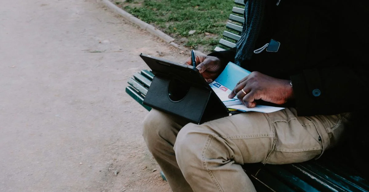Adulte utilisant une tablette et un bloc-notes sur un banc extérieur, multitâche.