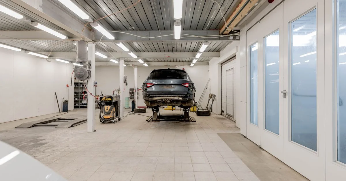 Garage bien éclairé avec une voiture sur un élévateur hydraulique prête à être réparée.