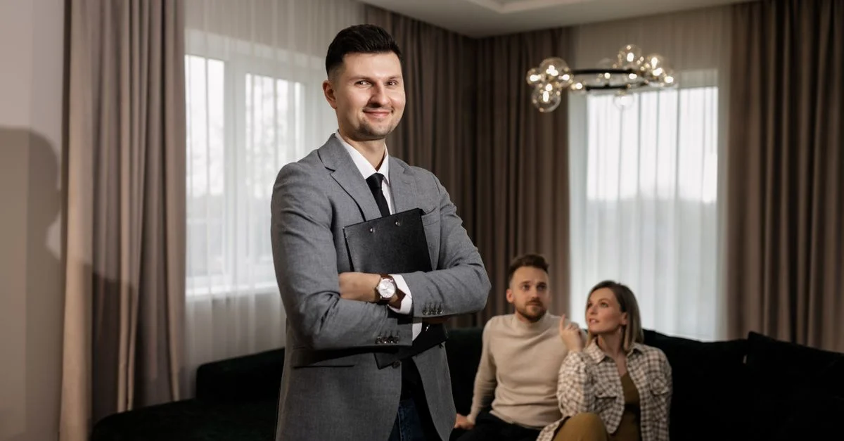 Agent immobilier souriant avec un tableau à l'intérieur, montrant une propriété à un couple.