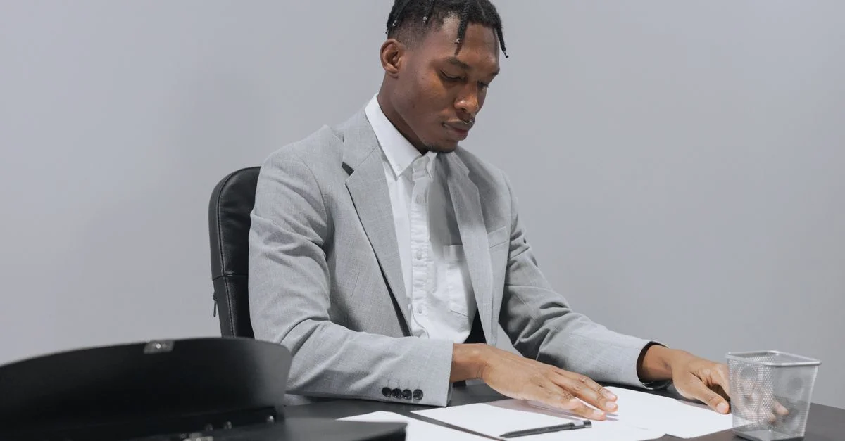 Homme d'affaires concentré en costume gris examinant des documents à un bureau, transmettant du professionnalisme.