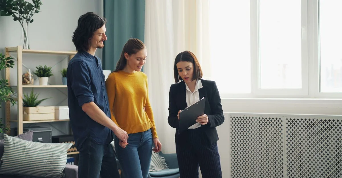 Un jeune couple discute des options d'achat de maison avec un agent immobilier dans une pièce moderne et lumineuse.