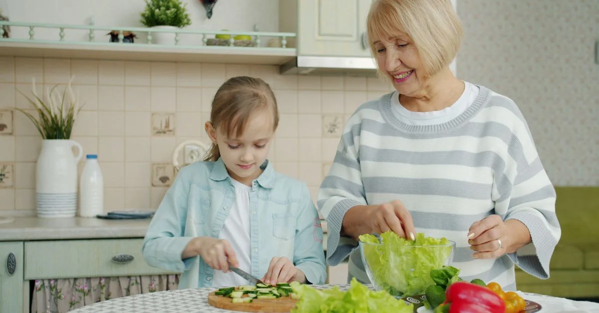 Une femme âgée et une jeune fille préparent des légumes dans une cuisine.