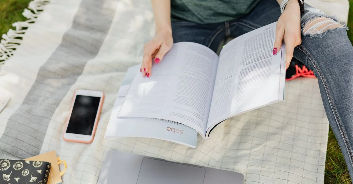 Une jeune femme est concentrée sur ses études en plein air avec son ordinateur portable et son smartphone, profitant du temps ensoleillé.