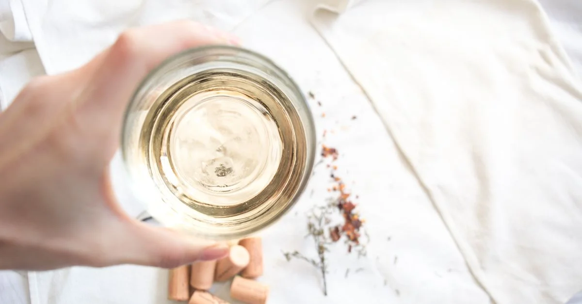 Une prise de vue plongeante d'une main tenant un verre de vin blanc avec des bouchons et un tissu blanc en arrière-plan.