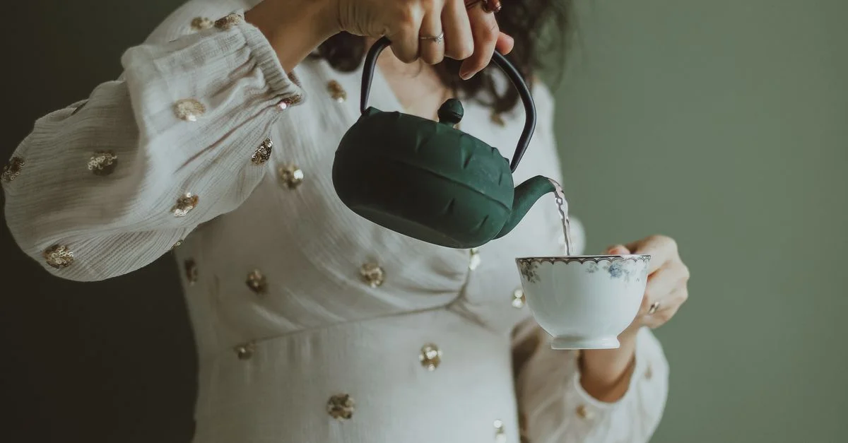 Une femme verse élégamment du thé d'une théière verte dans une tasse délicate à l'intérieur.