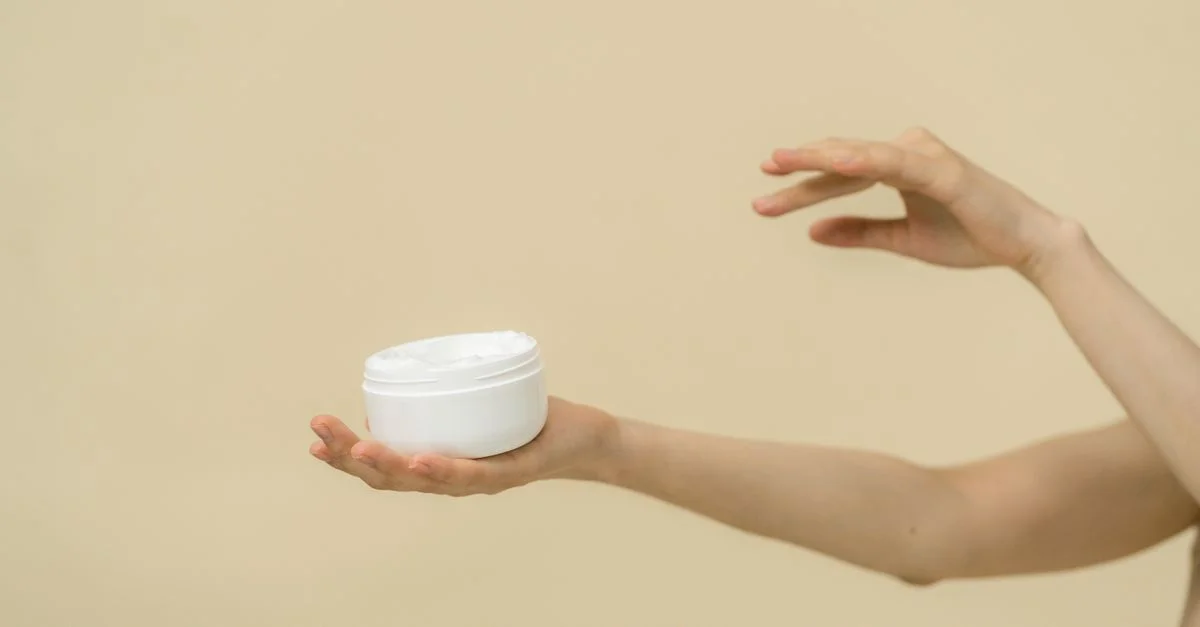 Image minimaliste de mains tenant un pot cosmétique, mettant en avant les soins de la peau et la beauté.