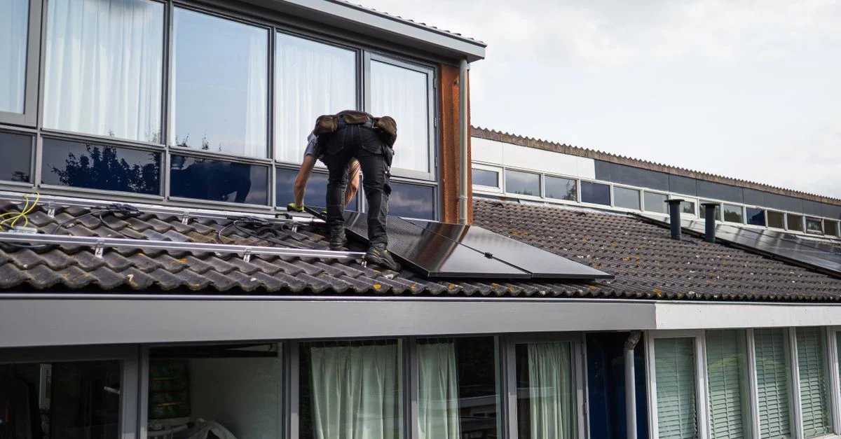 Technicien travaillant à l'installation de panneaux solaires sur un toit résidentiel pendant la journée.