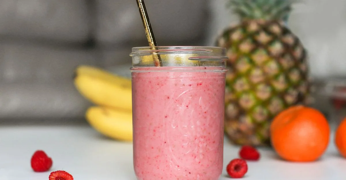 Un smoothie rose rafraîchissant à base de bananes, framboises et fruits tropicaux dans un bocal en verre.