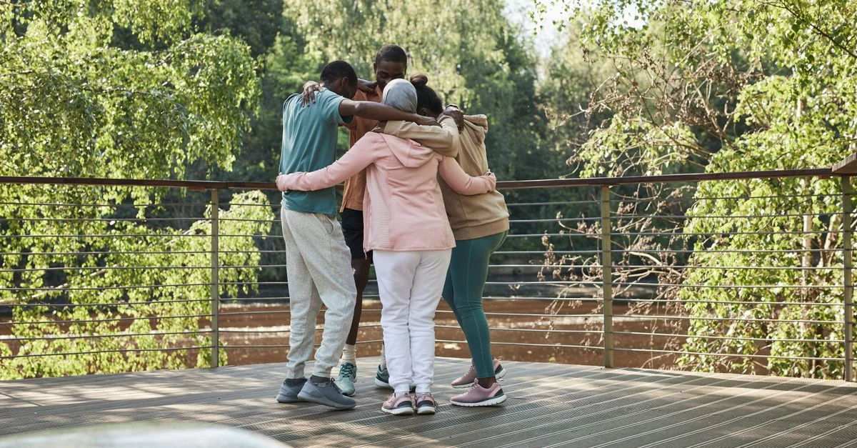 Des amis se blottissant dans une étreinte de groupe sur une terrasse ensoleillée entourée de verdure.