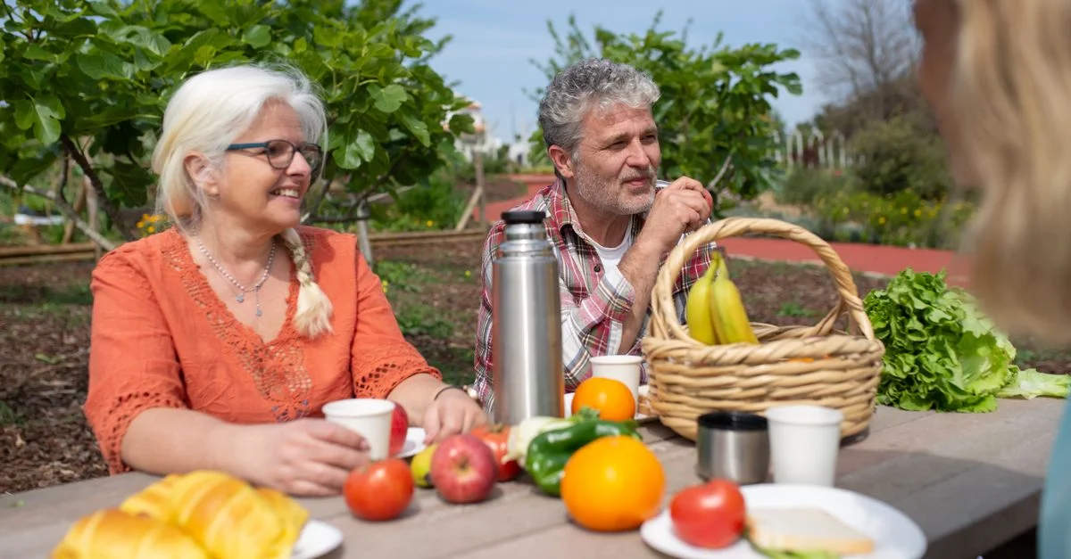 Un couple senior profite d'un pique-nique joyeux avec des fruits et légumes frais dans un cadre de jardin luxuriant.