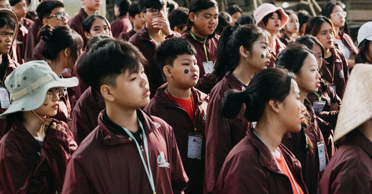 Un grand groupe d'adolescents portant des badges et des vestes lors d'un événement en plein air, attentifs et engagés.