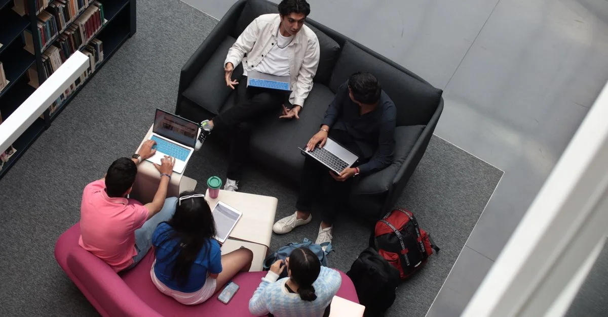 Un groupe d'étudiants divers utilisant des ordinateurs portables et des livres dans un cadre de bibliothèque, étudiant ensemble.