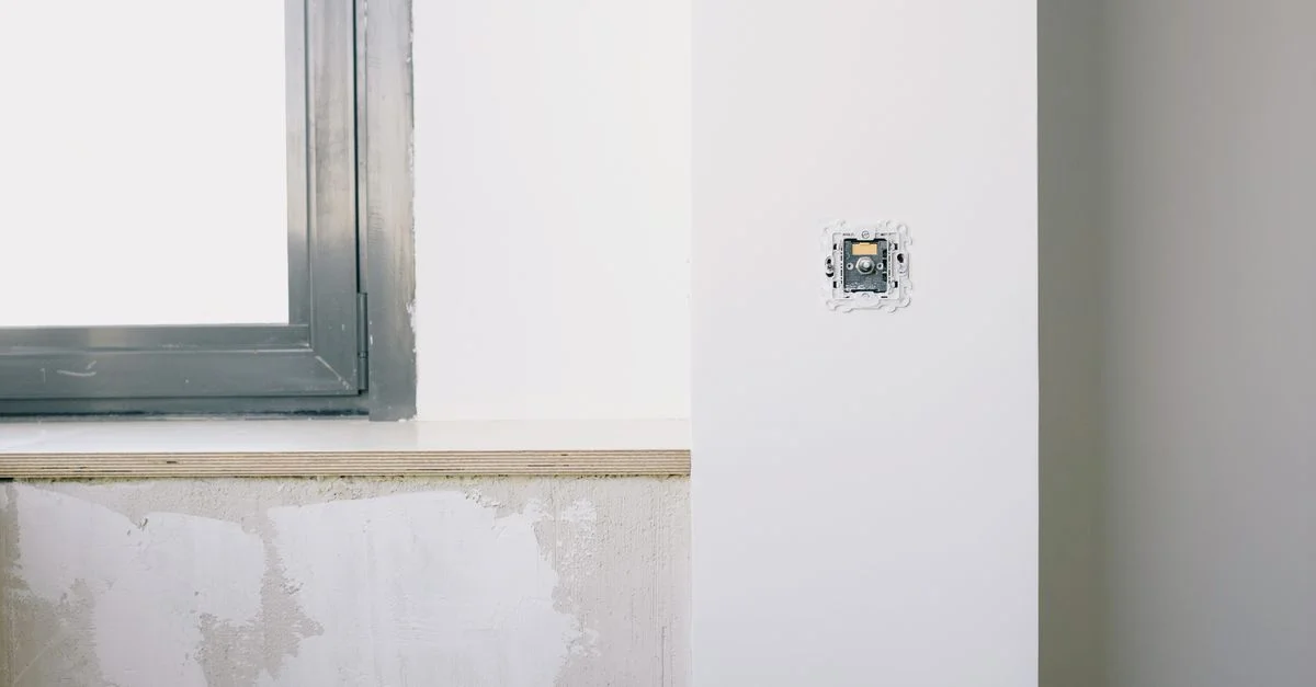 Une chambre moderne et minimaliste en rénovation montrant une installation d'interrupteur et une grande fenêtre.