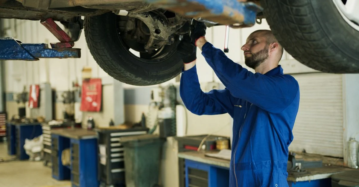 Mécanicien en bleu inspectant le châssis du véhicule dans un atelier professionnel.