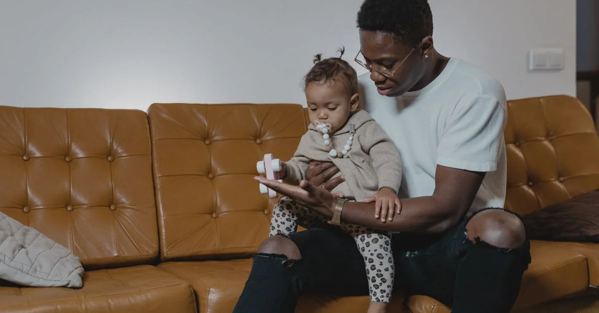 Un père tient tendrement son bébé sur un canapé en cuir. Cadre intérieur confortable capturant les liens familiaux.