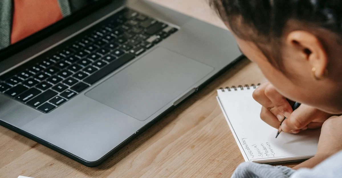 Enfant engagé dans l'éducation en ligne utilisant un ordinateur portable et prenant des notes dans un cahier.