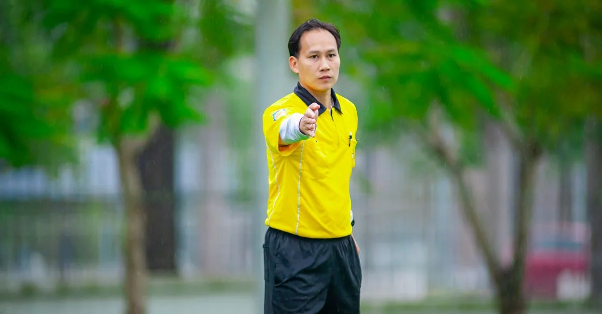 Un arbitre fait des signes lors d'un match de football à Hanoi, au Vietnam, sur un terrain vert.