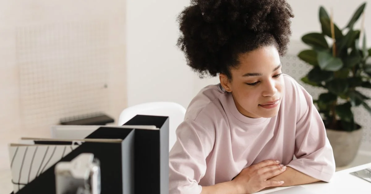 Femme afro-américaine avec des cheveux afro travaillant sur un ordinateur portable dans un bureau moderne.