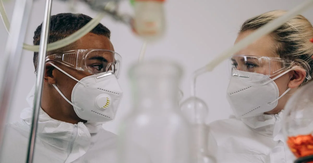 Deux scientifiques en combinaisons de protection et masques travaillant dans un laboratoire avec des équipements.