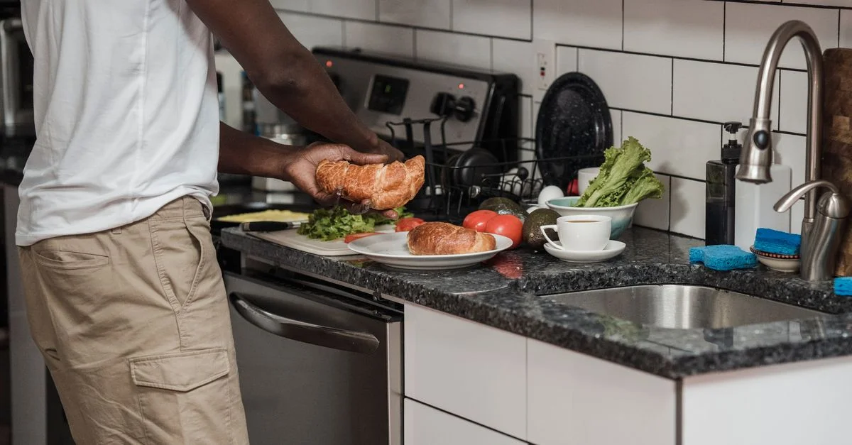Un homme prépare le petit-déjeuner dans une cuisine moderne avec des croissants frais et des légumes.