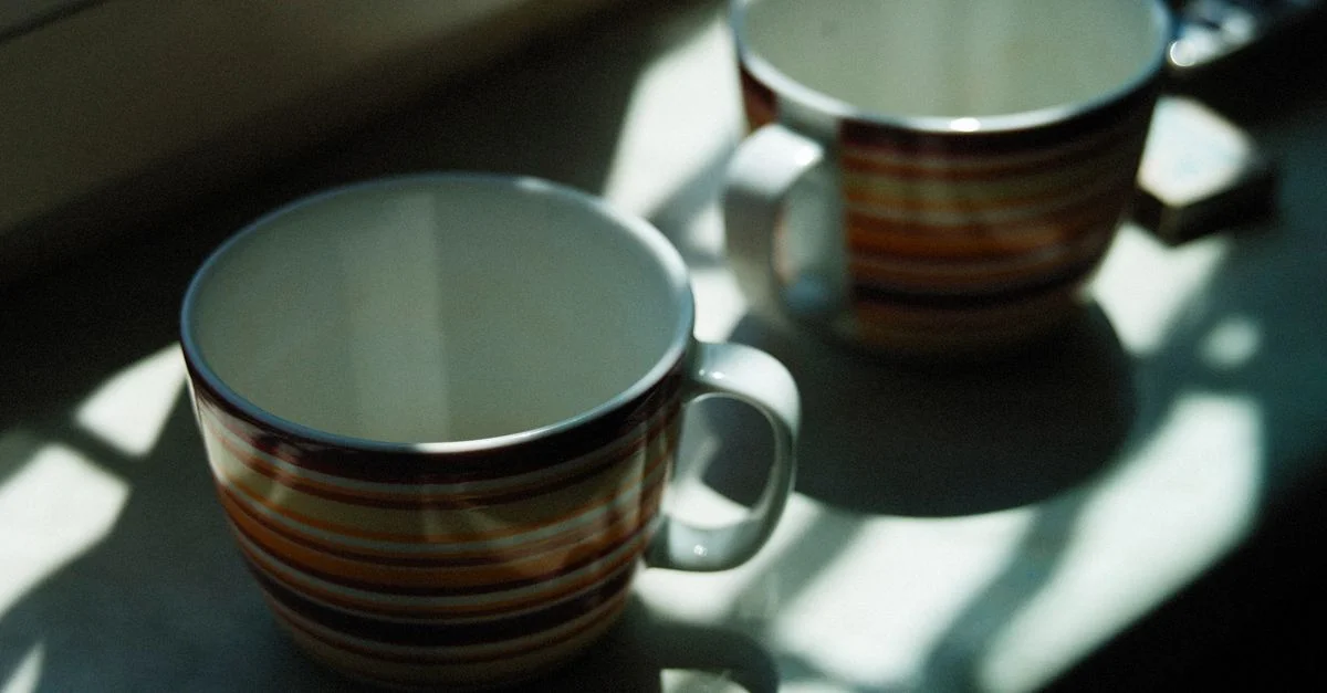 Deux tasses rayées baignées de soleil sur un rebord de cuisine créent une atmosphère chaleureuse.