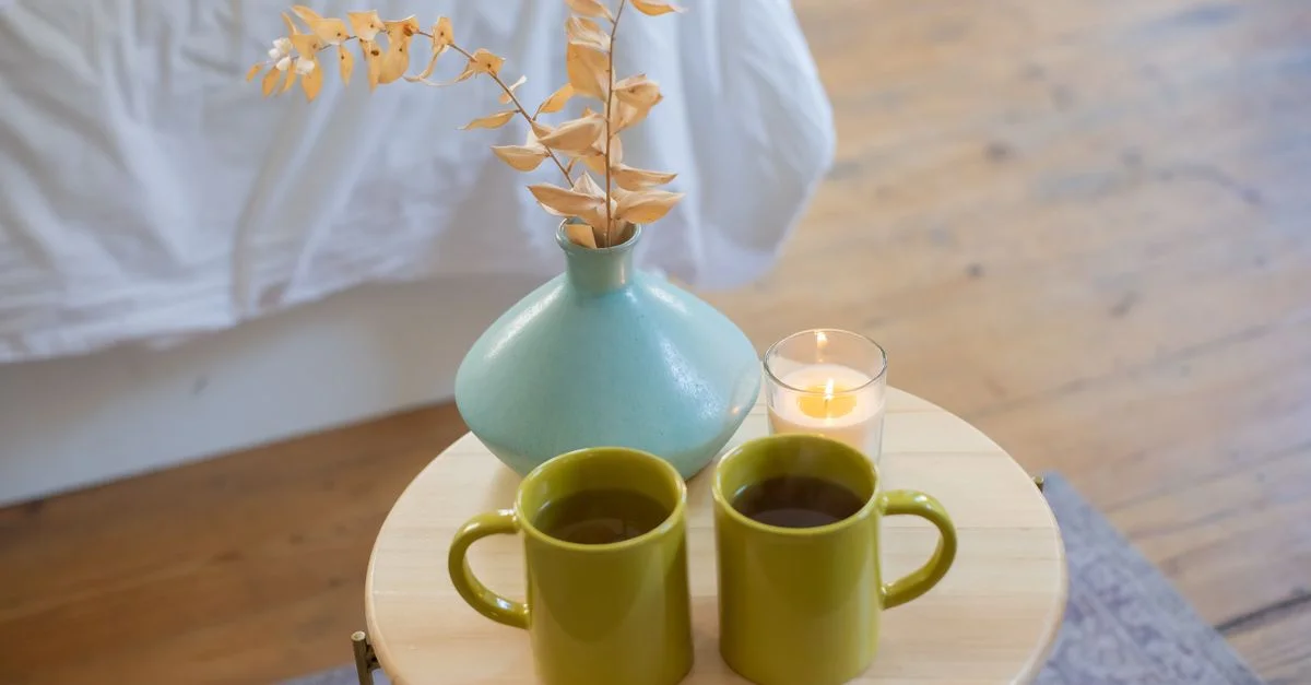 Deux tasses vertes sur une table avec un vase et une bougie, évoquant une atmosphère intérieure chaleureuse.