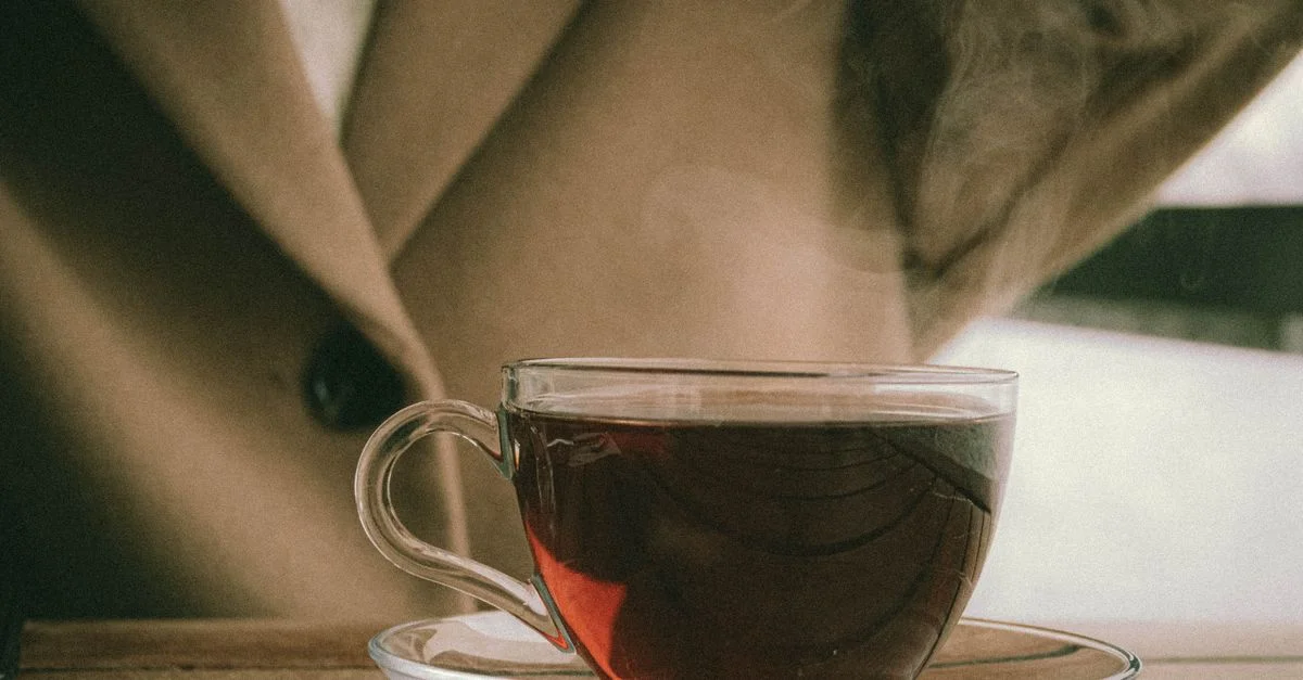 Une tasse à thé en verre remplie de thé noir fumant sur une table en bois.
