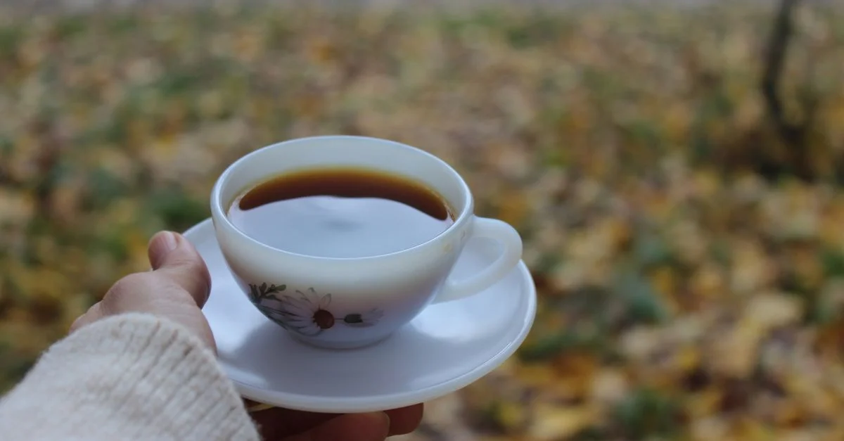 Une tasse de café cosy tenue en plein air parmi les feuilles d'automne, créant une atmosphère chaleureuse et accueillante.