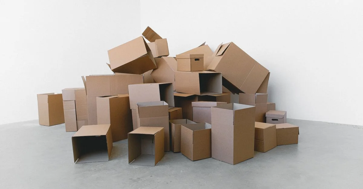 Une pile de boîtes en carton vides disposées sur un sol gris contre un mur blanc, parfaite pour des thèmes de déménagement.